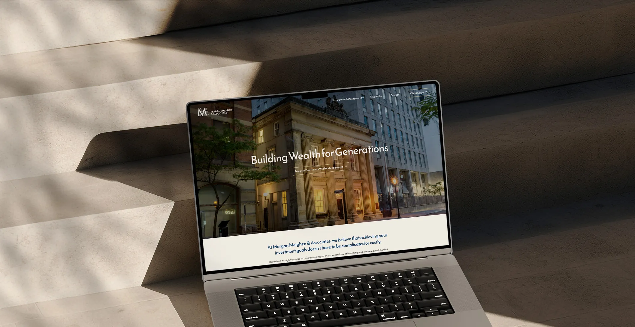 MM&A homepage hero on a laptop sitting on a staircase.