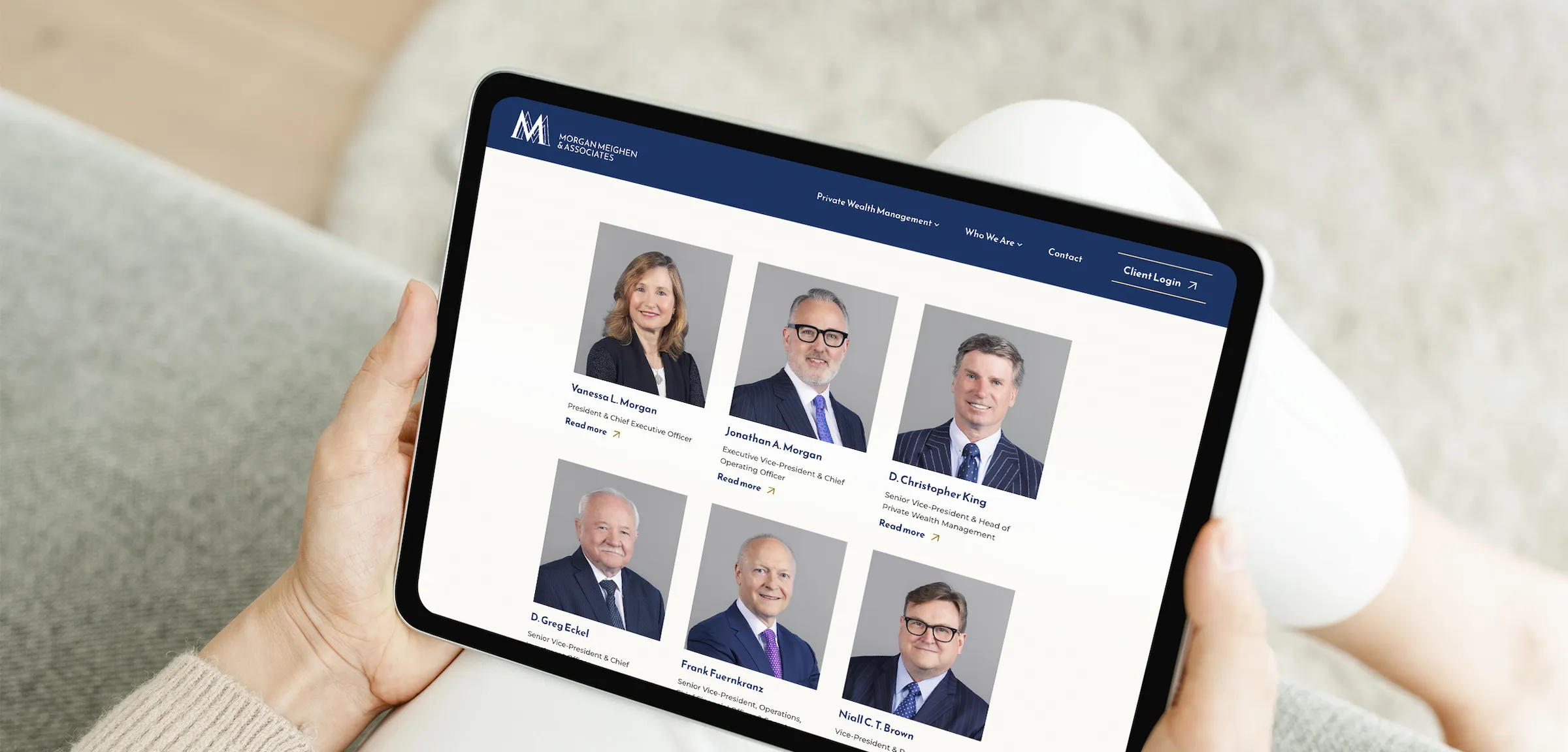 A woman sitting on a sofa holding a tablet device that shows the Our Team page.