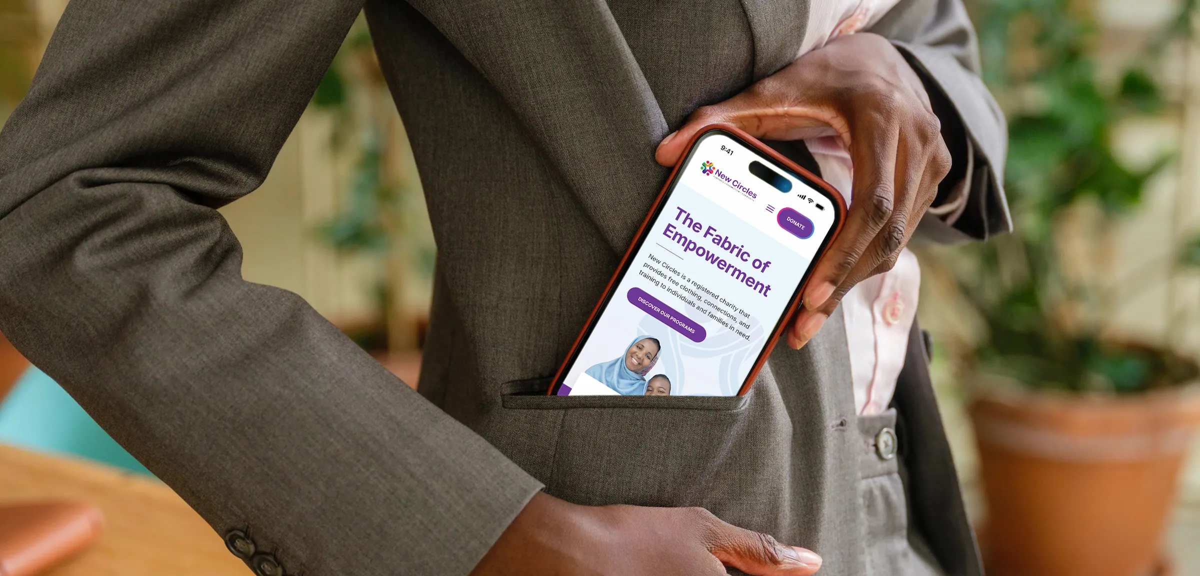 An up close shot of a woman dressed in buiness attire pulling a mobile device out of her pocket. The homepage of New Circles is on the device screen.